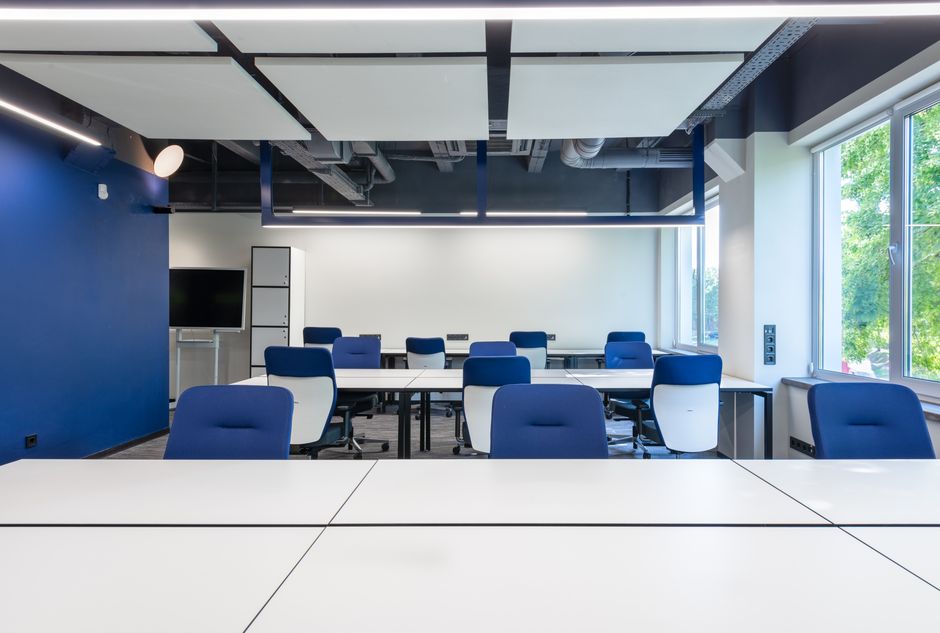 Various white desks with blue chairs placed in modern spacious workspace.
